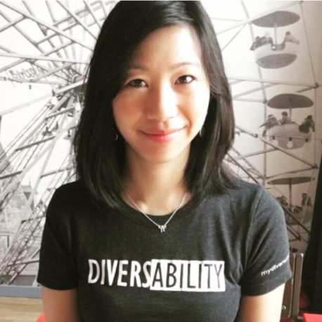 A headshot of a woman of Asian descent in front of a picture of a ferris wheel; her shirt says "DiversAbility"